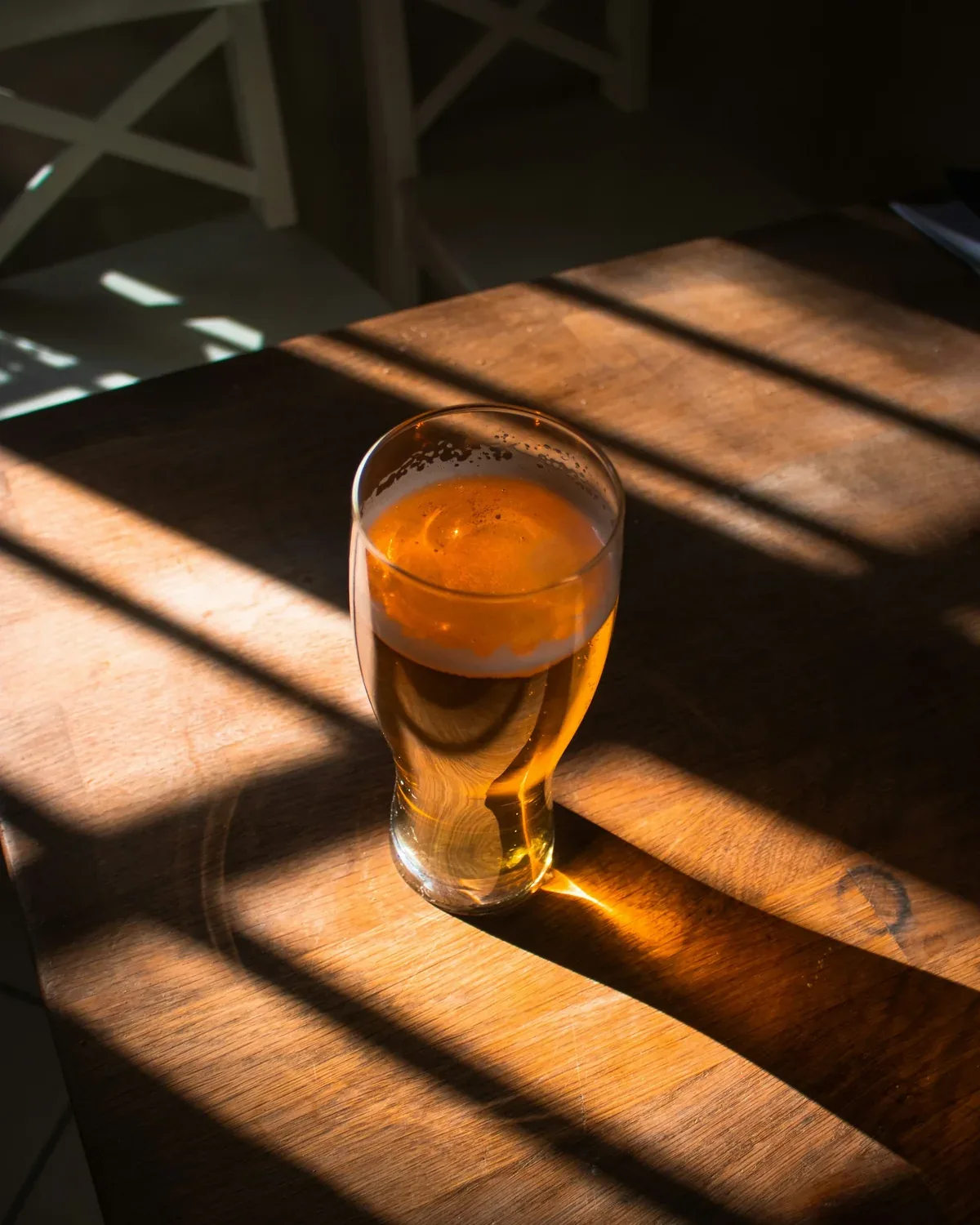 Verre de bière ambrée posé sur une table en bois, dans un rayon de soleil