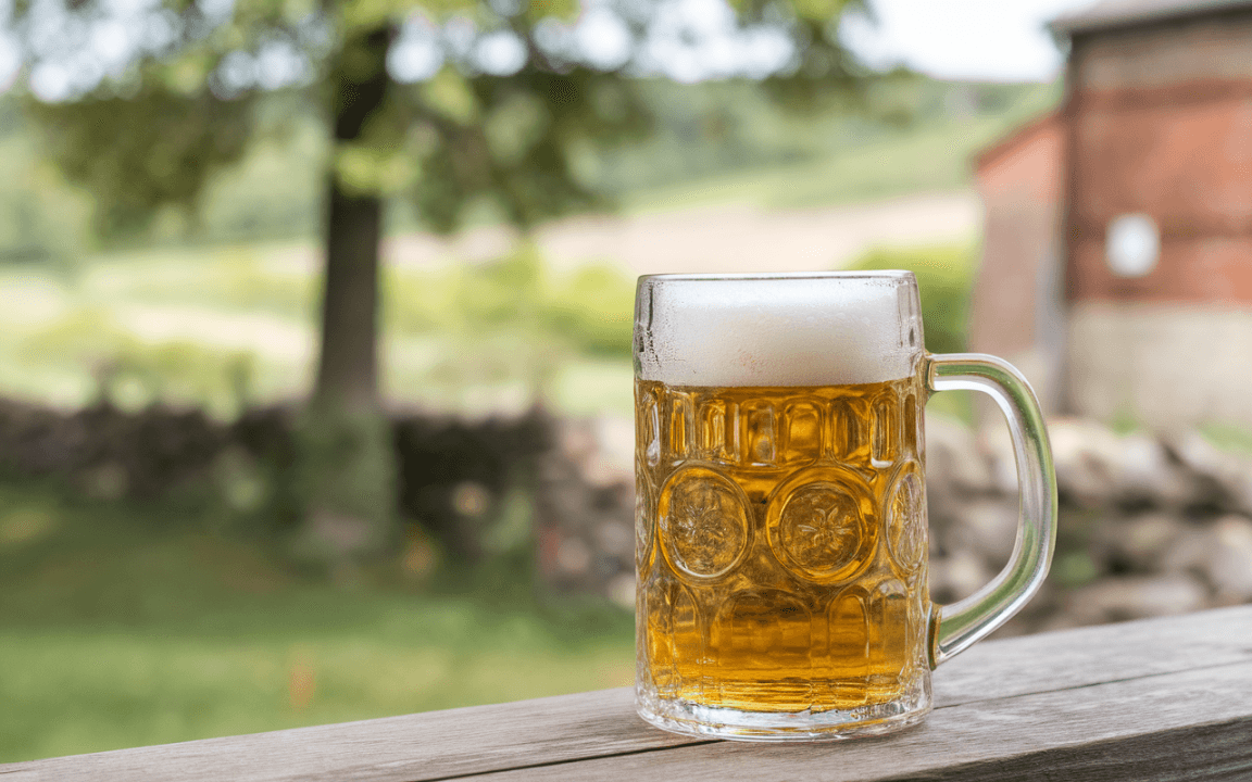 Une chope de bière pleine, mousseuse, posée sur une table en bois, avec un fond nature flou et verdoyant.
