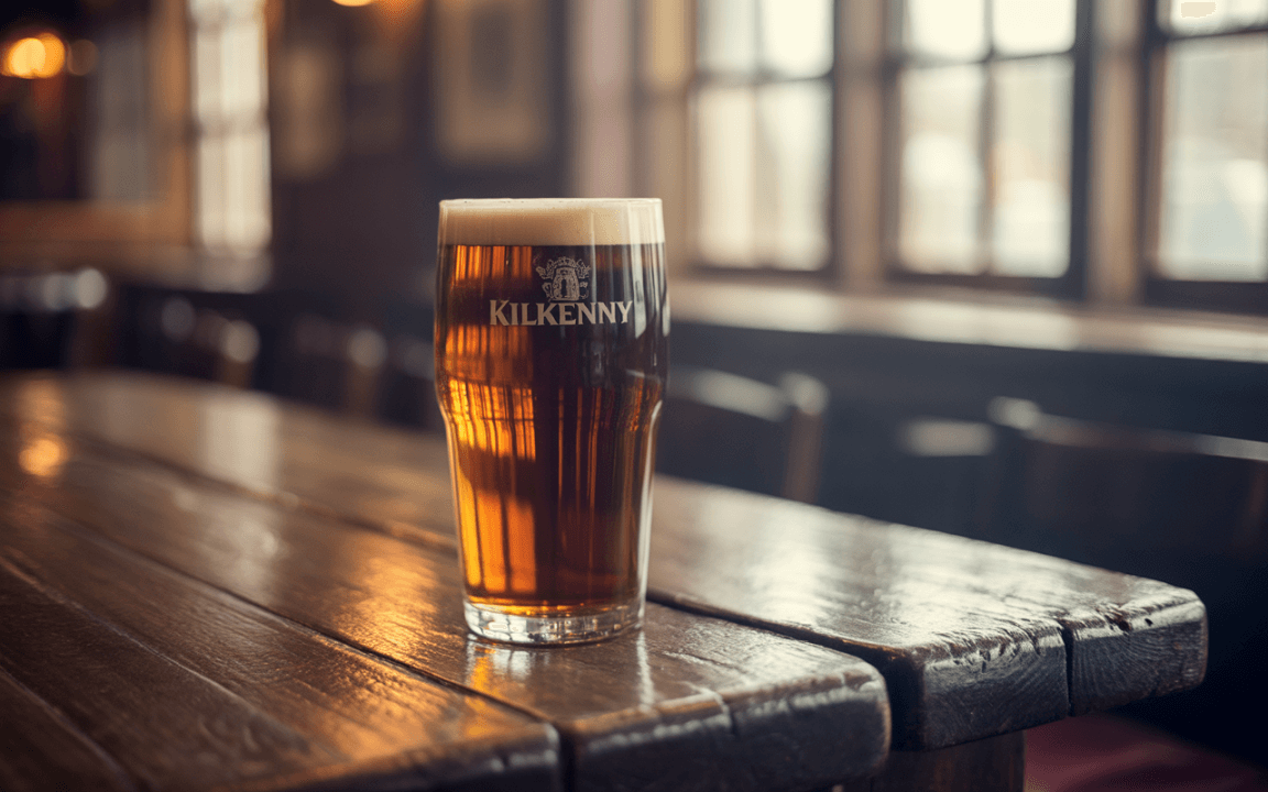 Un verre de bière Kilkenny posé sur une table en bois, avec un fond flou de pub chaleureux et éclairé.