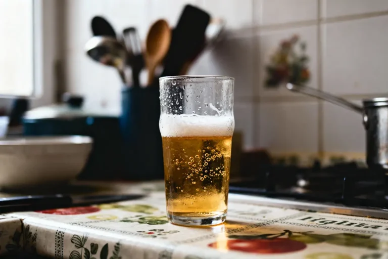 Verre de bière dorée avec mousse sur une table de cuisine décorée de motifs colorés.