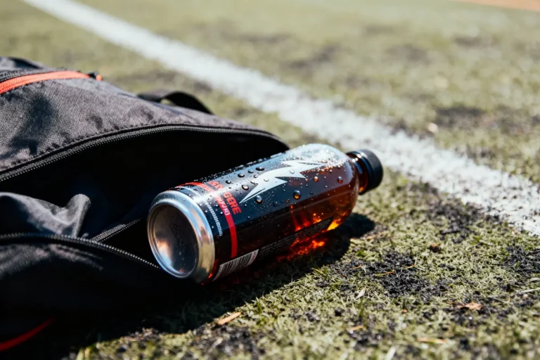 Bouteille énergétique sur gazon synthétique près d'un sac ouvert, sous le soleil.