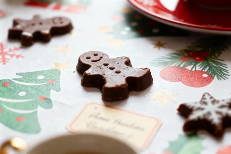 Chocolat en forme de bonhomme en pain d'épices sur nappe festive, motifs sapin et flocons de neige.
