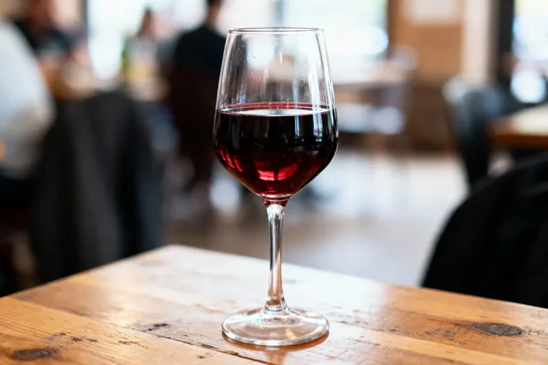 Verre de vin rouge sur une table en bois, arrière-plan flou d'un restaurant.