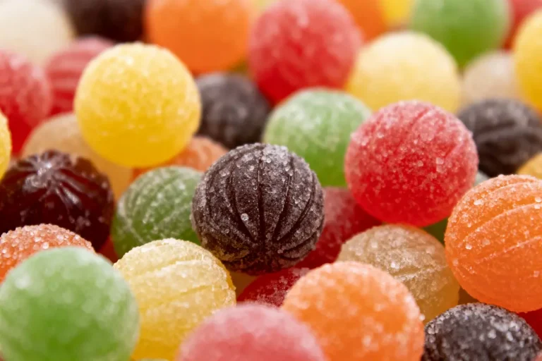 Boules de bonbons colorées, rouges, vertes, orange, enrobées de sucre, entassées, éclairage doux, macro.