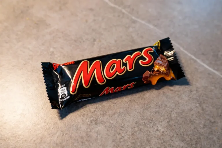 Barre chocolatée Mars ouverte, posée sur une surface grise, avec caramel visible. Emballage noir et rouge.