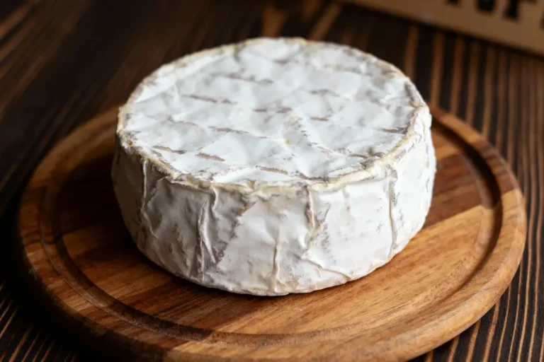 Fromage à croûte blanche posé sur une planche en bois sombre, texture plissée visible.