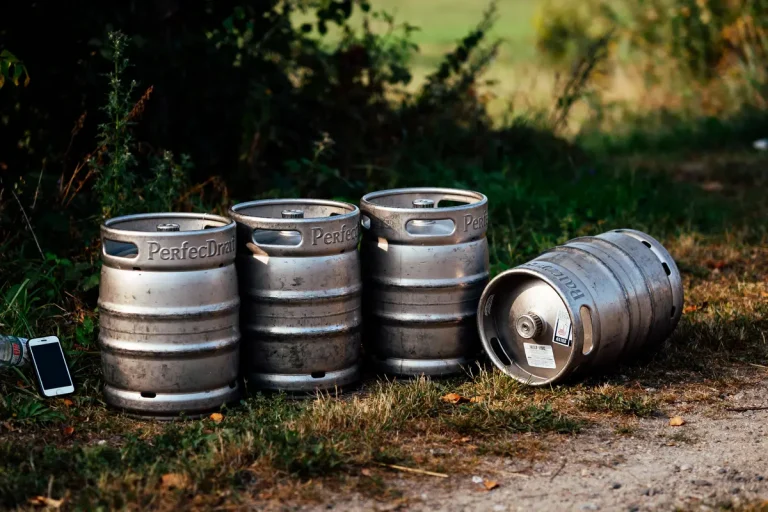 Quatre fûts de bière métalliques posés sur l'herbe près d'un téléphone portable, en extérieur.