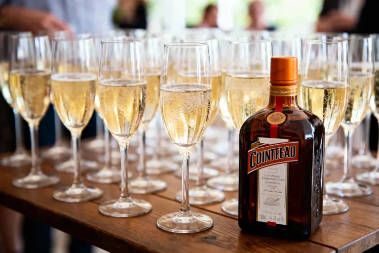 Bouteille de Cointreau entourée de flûtes de champagne sur une table en bois lors d'un événement.
