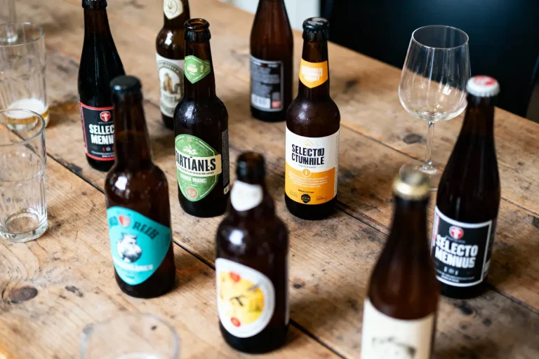 Bouteilles de bière variées sur une table en bois, entourées de verres vides et un verre à pied élégant.