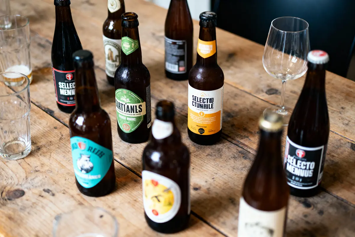 Bouteilles de bière variées sur une table en bois, entourées de verres vides et un verre à pied élégant.