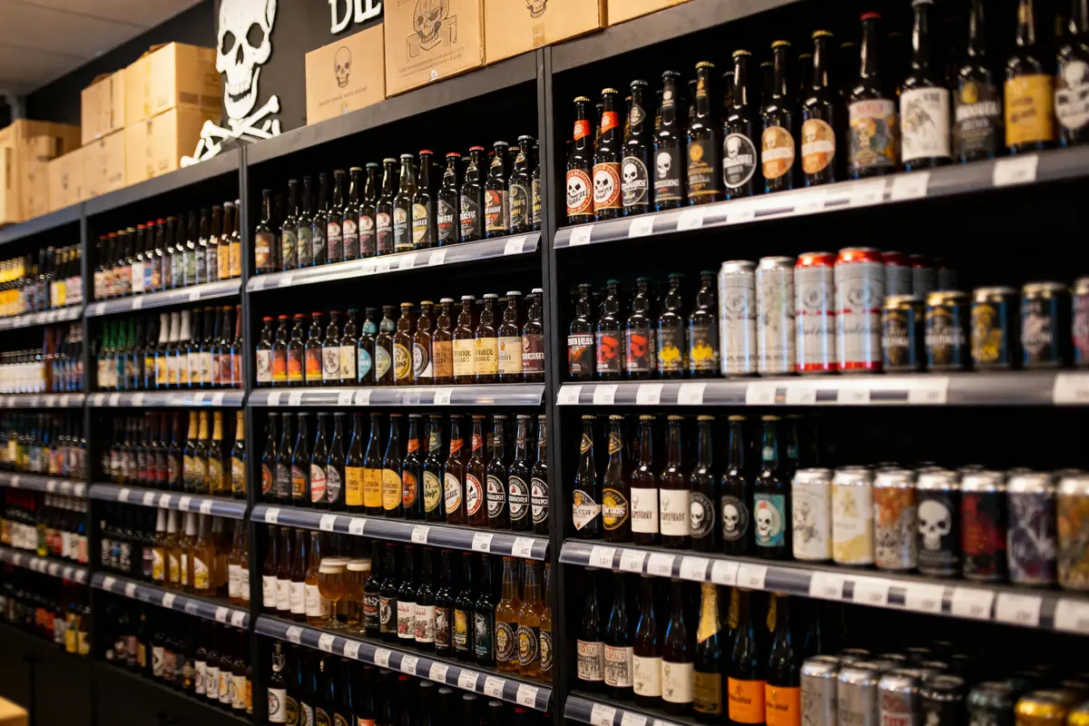 Rayons d'un magasin avec des bouteilles et canettes de bière variées, décoré de motifs de crânes.