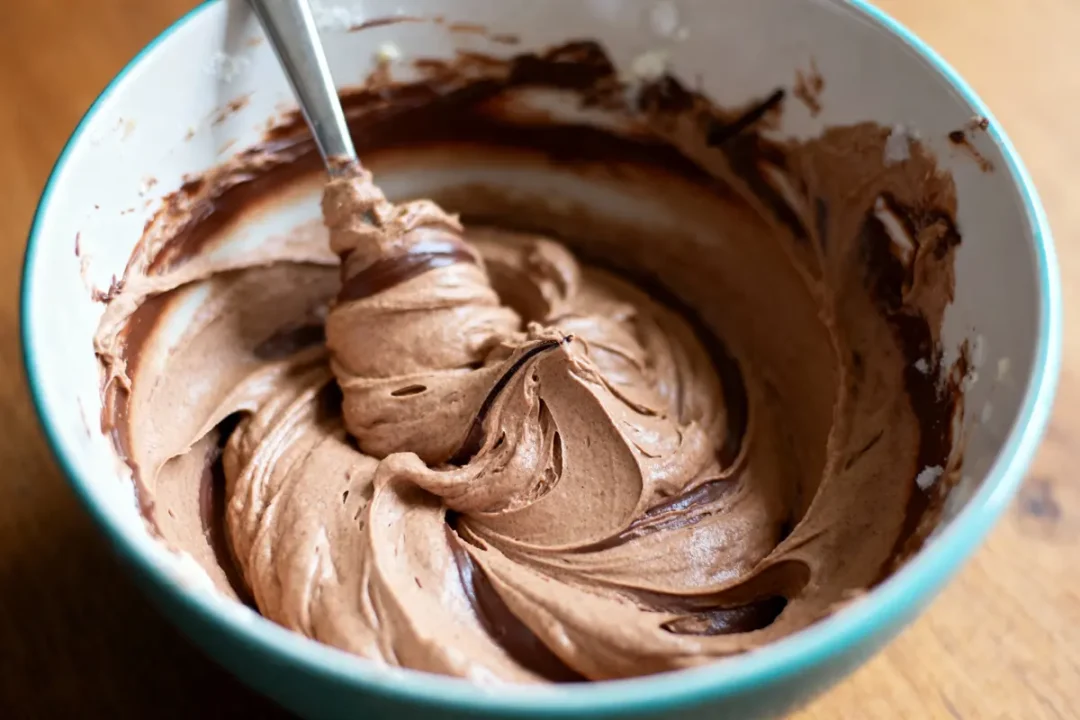 Bol contenant une pâte à gâteau au chocolat, bien mélangée avec une cuillère en métal.
