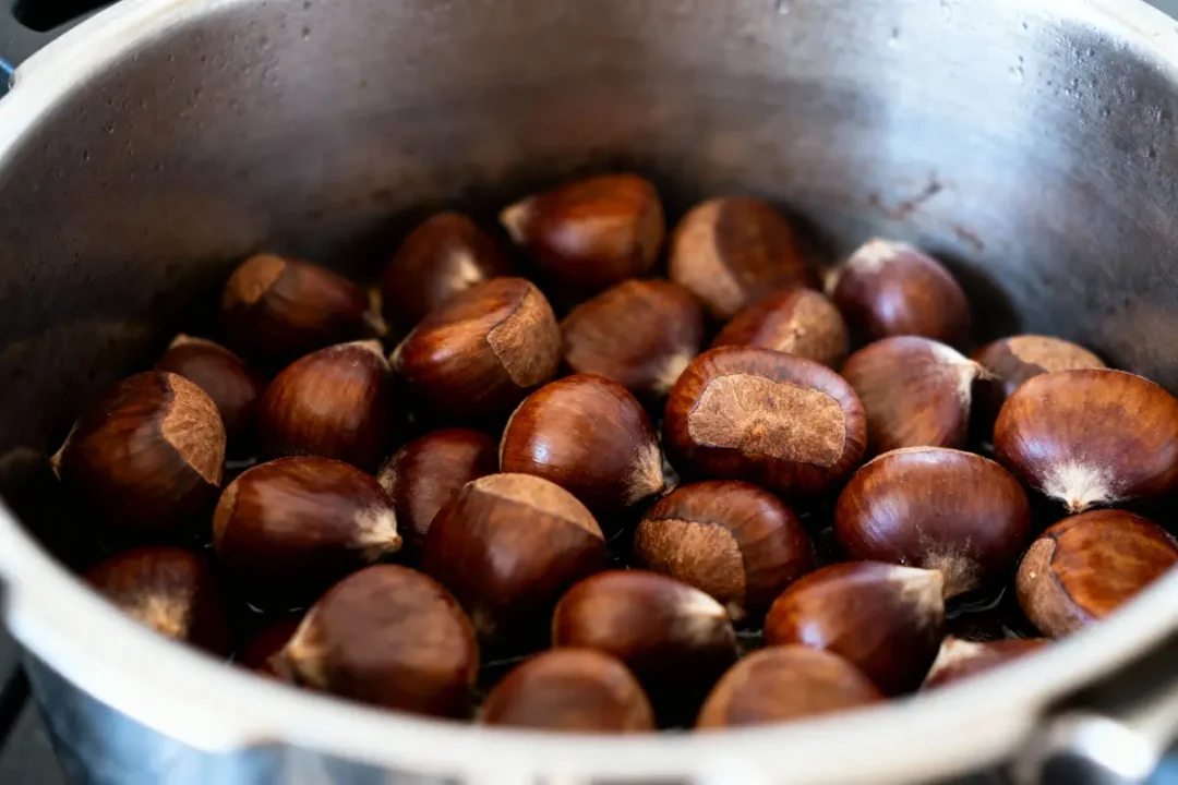Châtaignes brunes crues dans une casserole en métal, prêtes à être cuites ou grillées.