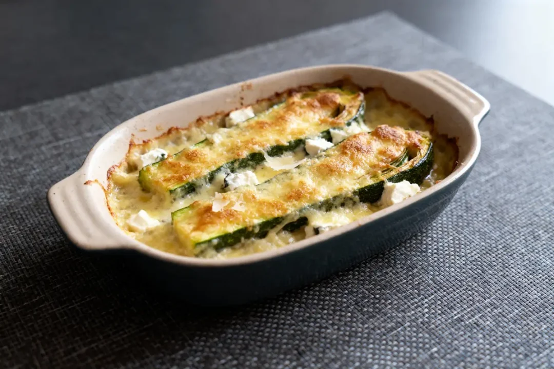 Gratin de courgettes au fromage doré, dans un plat en céramique, sur nappe grise.