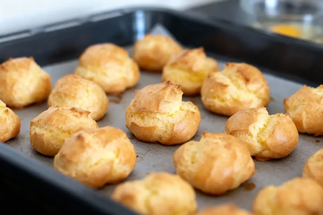 Choux dorés et soufflés cuits sur une plaque à pâtisserie recouverte de papier cuisson.