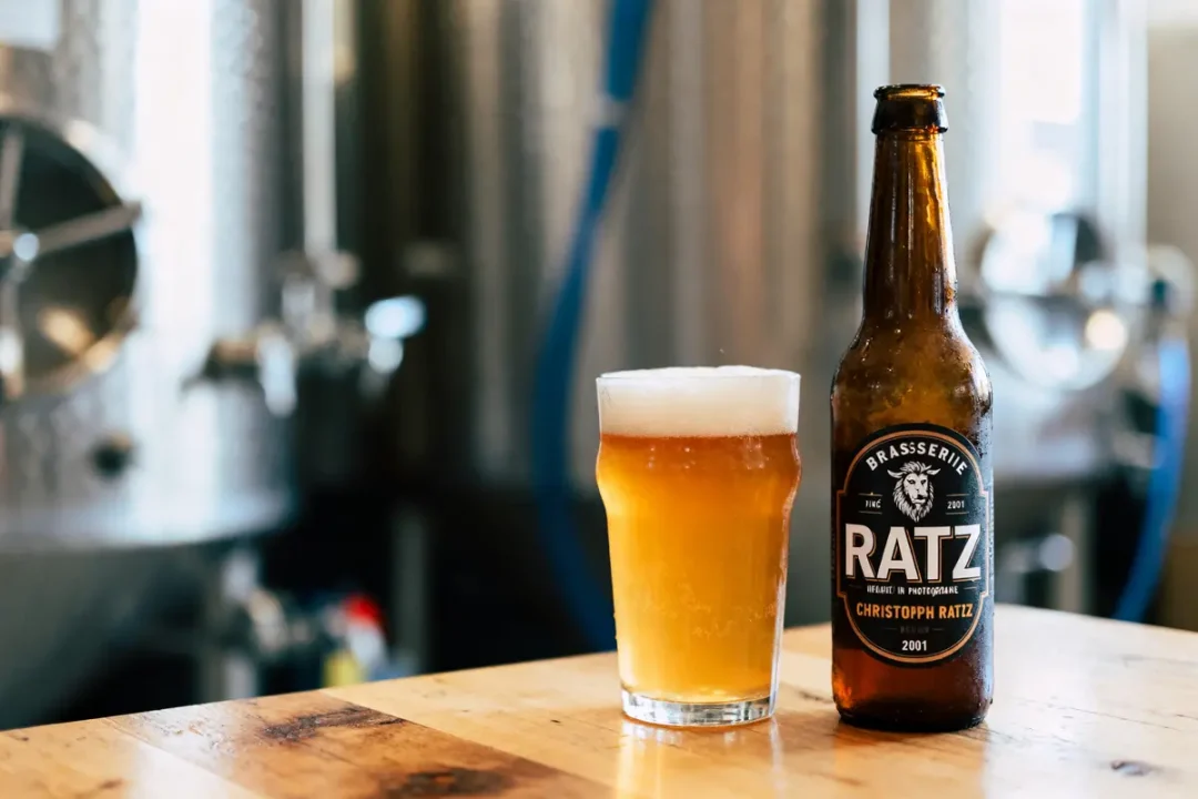 Bouteille et verre de bière Ratz sur table en bois, avec cuves en arrière-plan dans une brasserie.