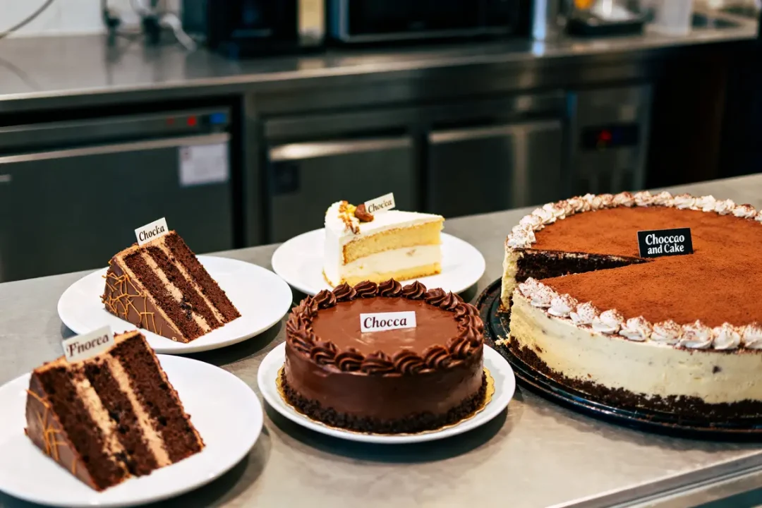 Assortiment de gâteaux variés sur un comptoir, incluant chocolat et tiramisu, dans une pâtisserie moderne.