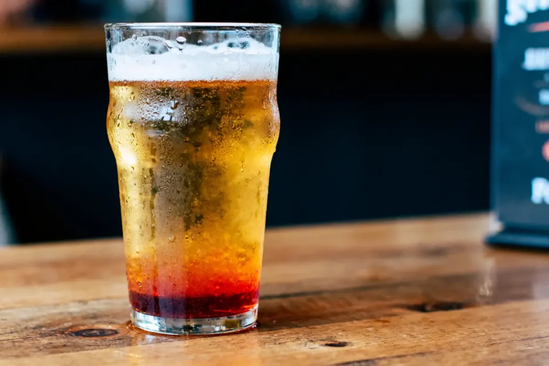 Verre de bière avec sirop rouge, posé sur une table en bois, arrière-plan flou.