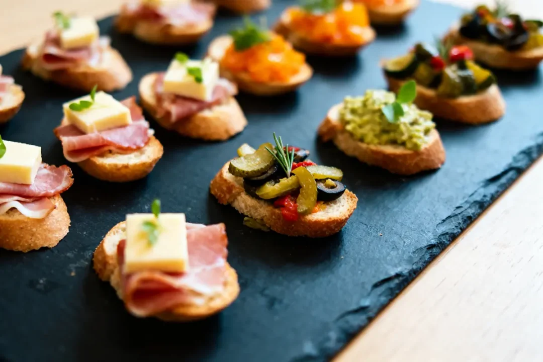 Plateau de crostinis variés avec fromage, jambon, olives et garnitures colorées sur planche ardoise.