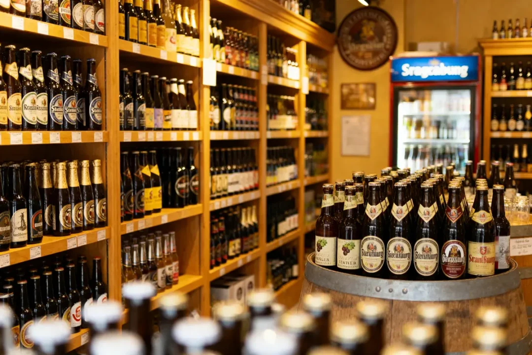 Rayonnages remplis de bouteilles de bière variées dans un magasin, avec réfrigérateur en arrière-plan.