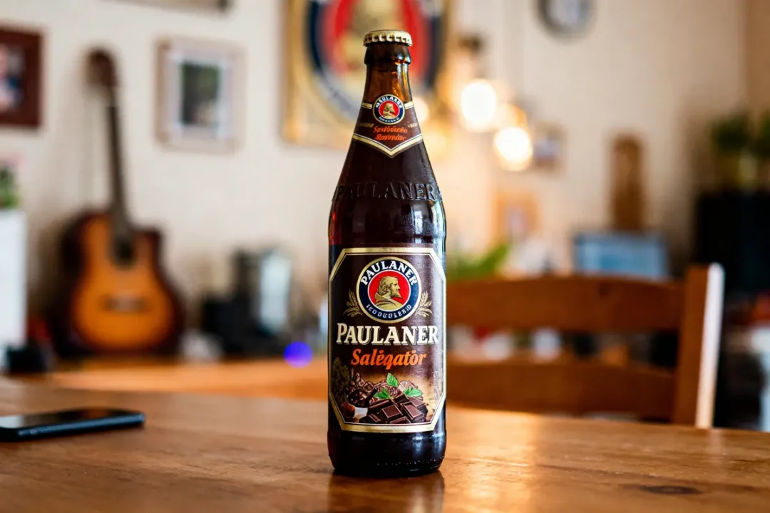 Bouteille de bière Paulaner Salégator sur table en bois, arrière-plan flou avec guitare et lumière.