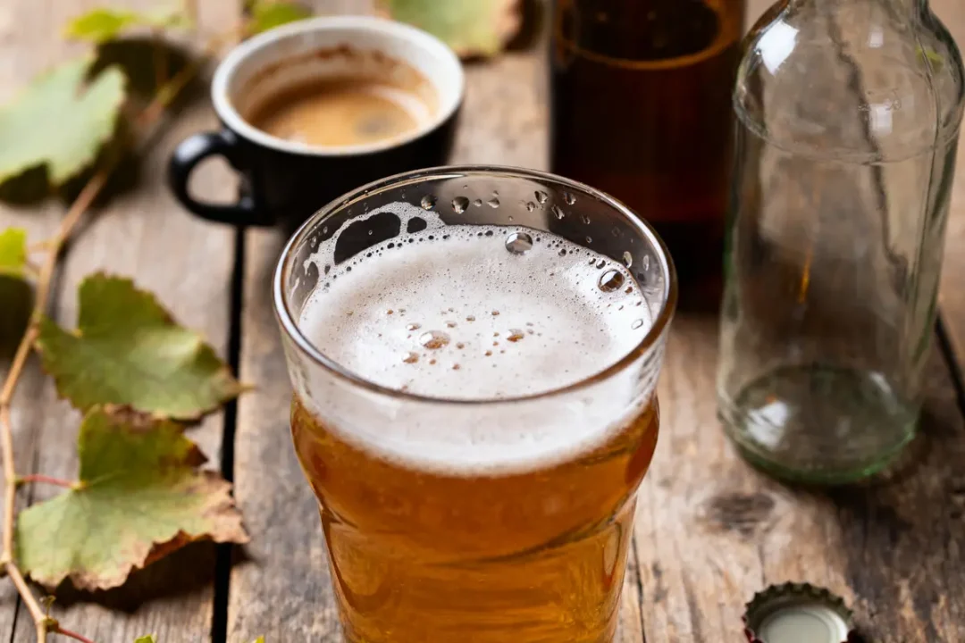 Verre de bière artisanale locale sur table en bois avec tasses et bouteilles.
