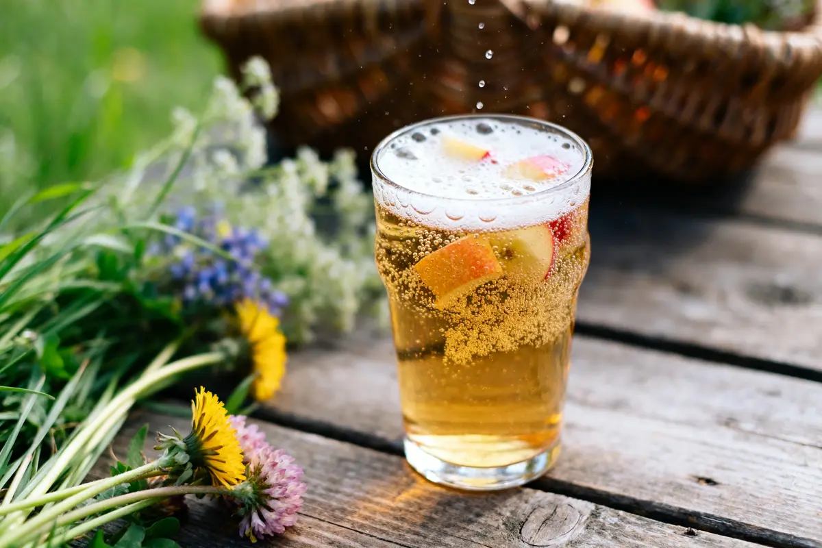 Verre de bière de printemps pétillante avec morceaux de fruits, fleurs en arrière-plan