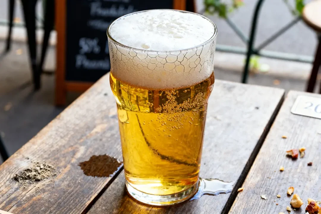Verre de bière maltée mousseuse sur table en bois dans un café extérieur
