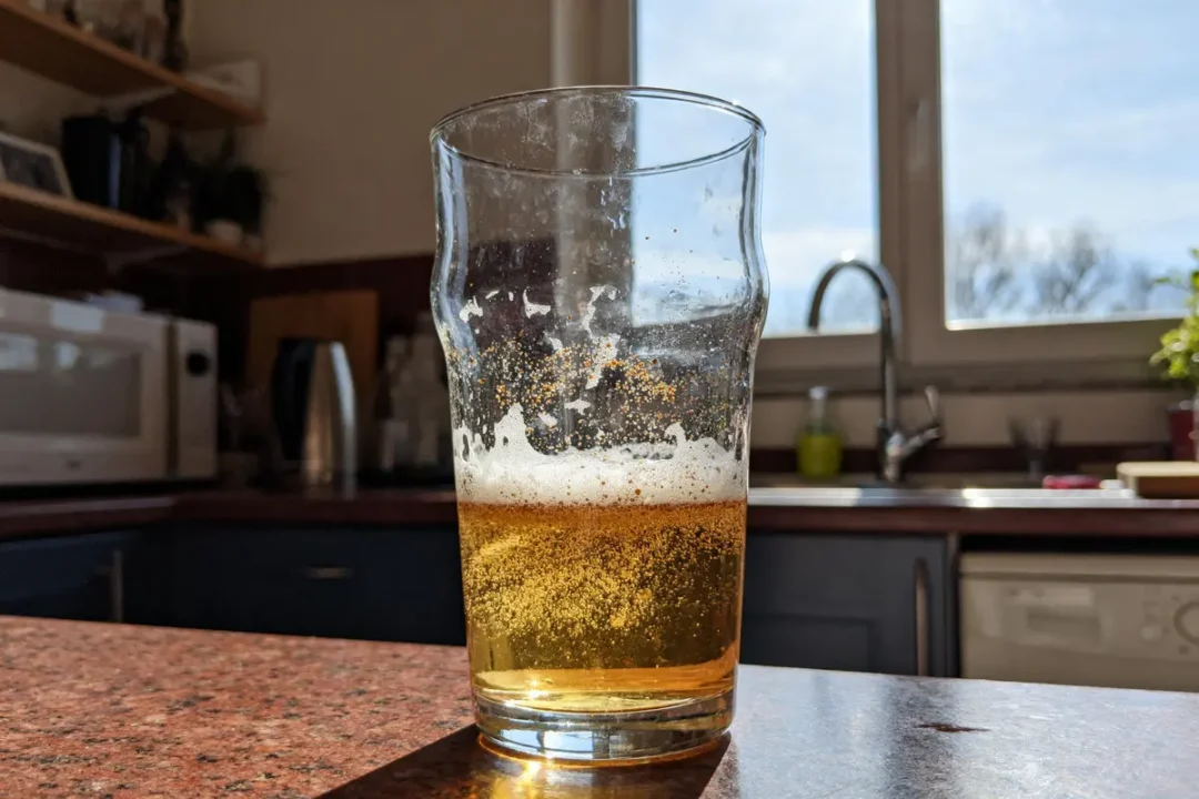 Verre de bière sèche partiellement vide dans une cuisine ensoleillée.
