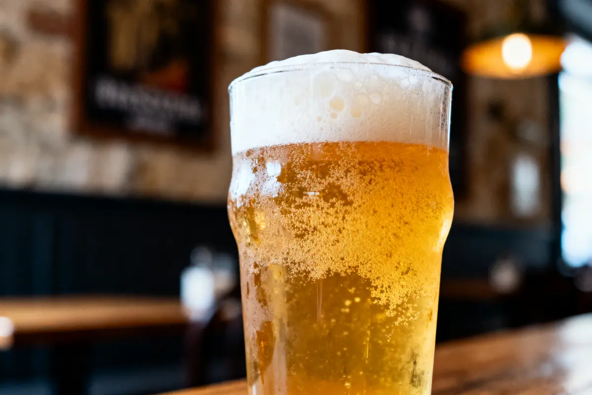 Verre de bière mousseuse sur table en bois dans un bar au décor flou.
