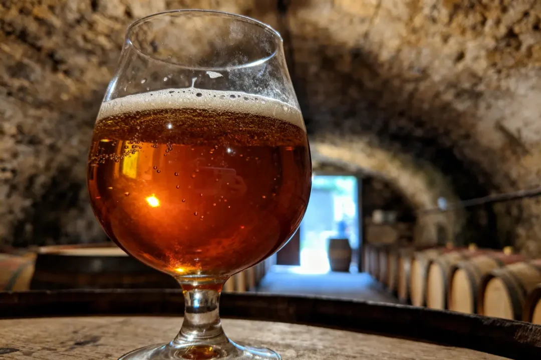 Verre de bière ambrée sur tonneau dans une cave voûtée mal éclairée.