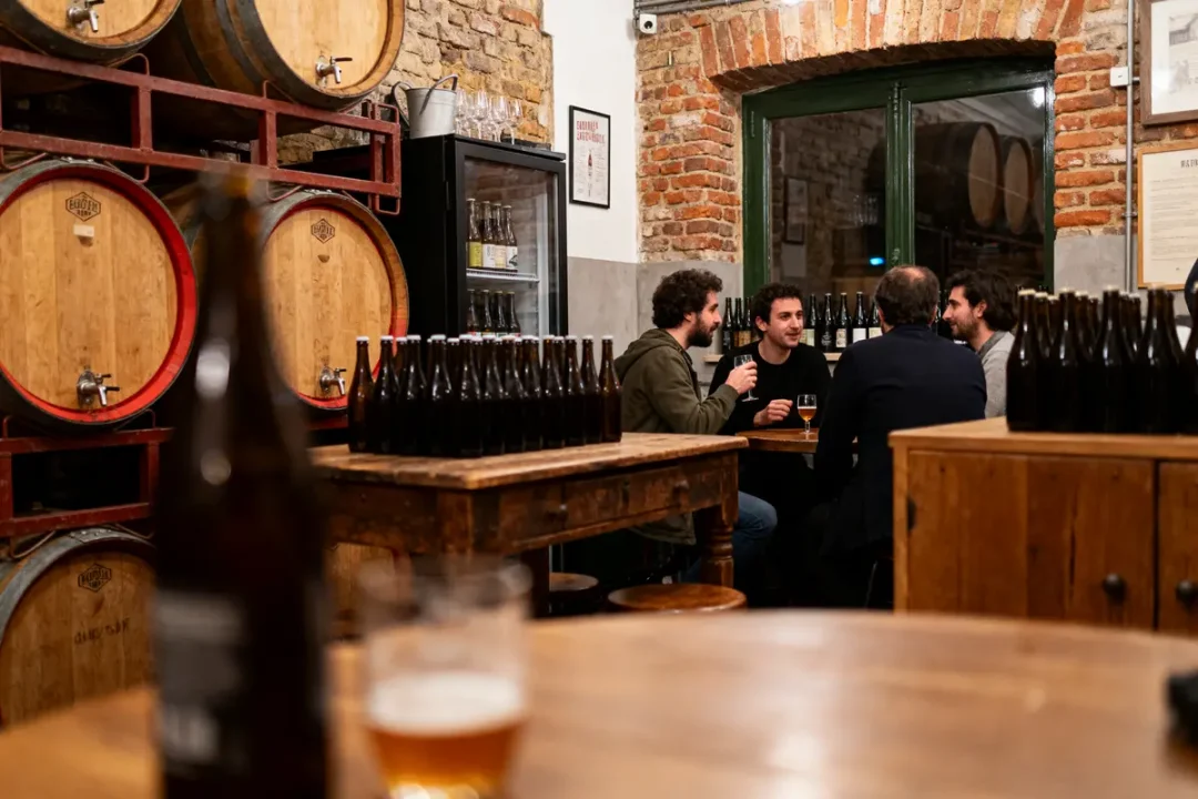 Un groupe d'hommes discute dans une brasserie rustique avec fûts et bouteilles de bière.
