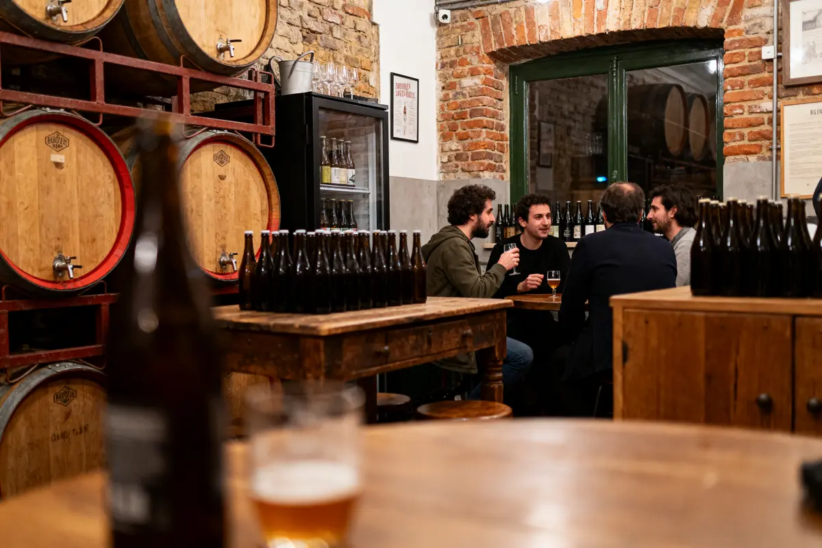 Un groupe d'hommes discute dans une brasserie rustique avec fûts et bouteilles de bière.
