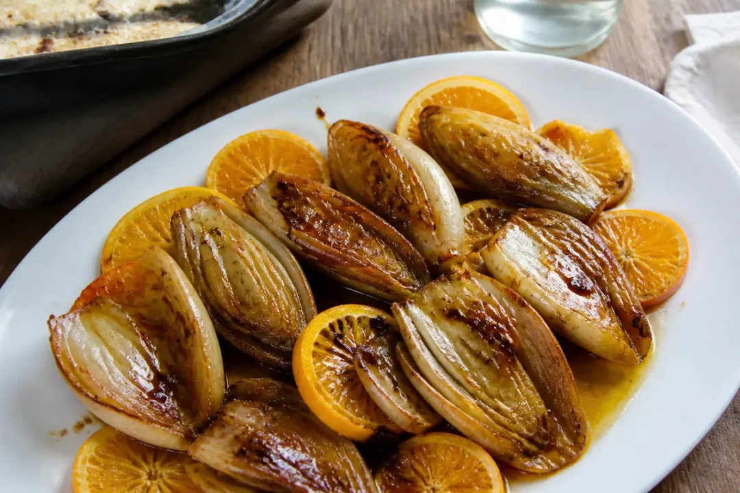 Assiettes d'endives caramélisées aux agrumes, présentées sur un plat blanc, avec un verre d'eau.