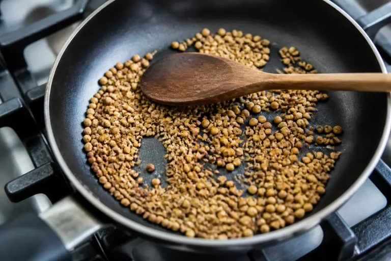 Graines de coriandre grillées dans une poêle avec cuillère en bois sur cuisinière.