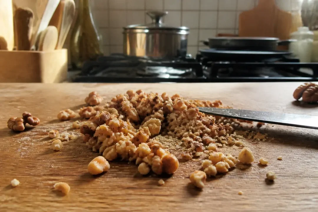 Noix hachées sur planche en bois dans une cuisine avec couteau et ustensiles en arrière-plan.