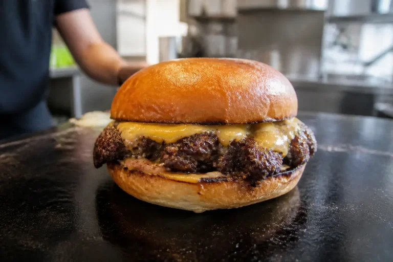 Un hamburger avec fromage fondu sur pain brioché dans une cuisine professionnelle.