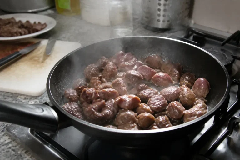 Boulettes de viande mijotant dans une poêle noire sur une cuisinière, vapeur s'élevant. Fond cuisine floue.